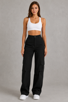 Woman wearing a white tank top and black cargo pants on a gray background