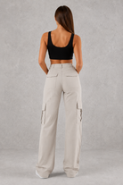 Woman wearing beige cargo pants and black top on a gray background