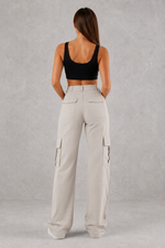Woman wearing beige cargo pants and black top on a gray background