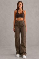 Woman wearing a brown sports bra and cargo pants against a gray background