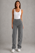 Woman wearing gray cargo pants and a white tank top against a gray background