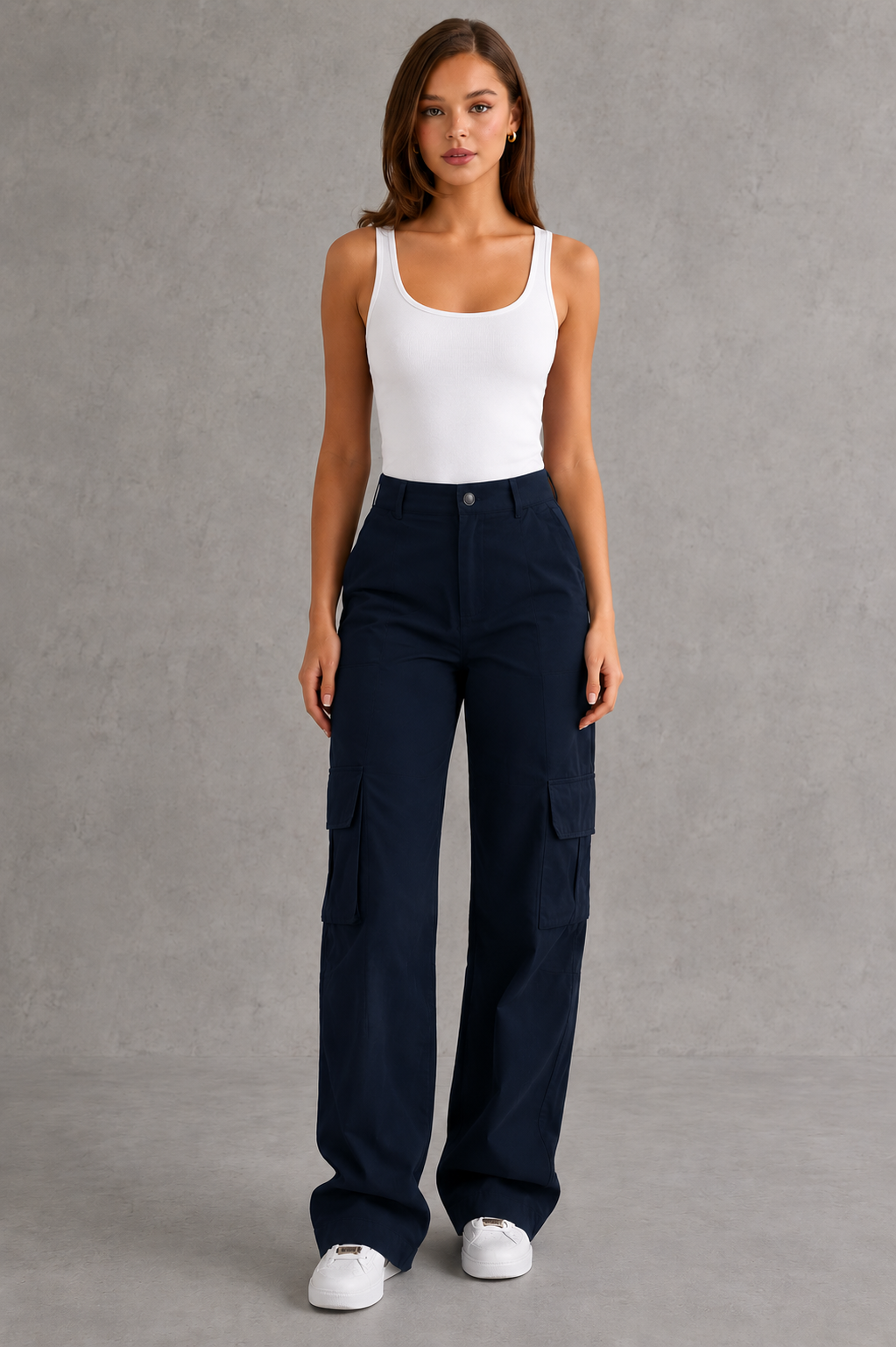 Woman wearing a white tank top and navy cargo pants against a gray background