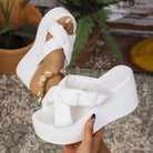 White platform sandals held by a hand with a blurred outdoor background