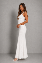 A woman modeling a white sleeveless maxi dress with a textured, dotted lace-like pattern, photographed against a neutral gray studio backdrop.