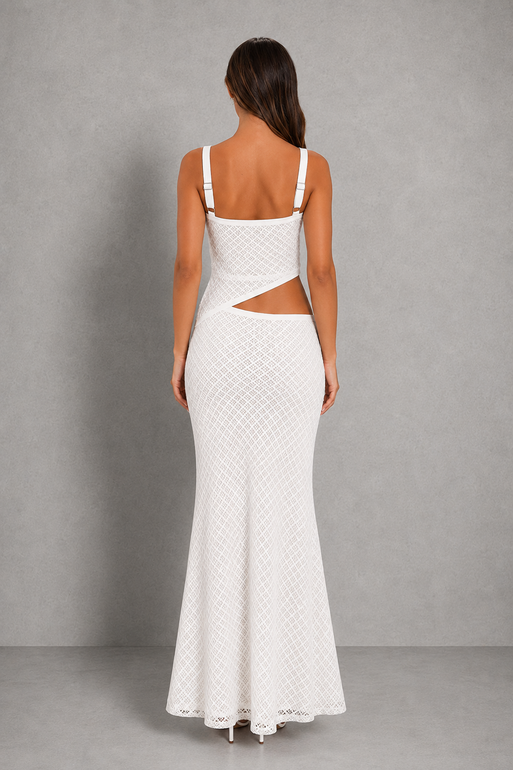 A woman viewed from the back wearing a white sleeveless maxi dress with thin shoulder straps, a square neckline, and a side cutout at the waist, photographed against a plain gray studio backdrop.