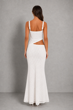 A woman viewed from the back wearing a white sleeveless maxi dress with thin shoulder straps, a square neckline, and a side cutout at the waist, photographed against a plain gray studio backdrop.