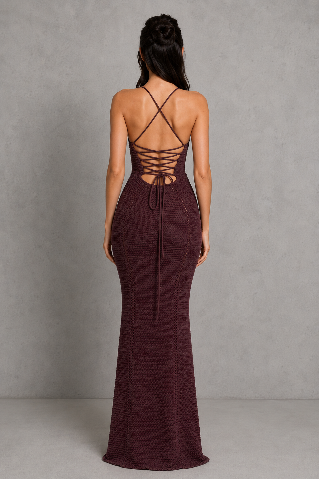 Woman wearing a burgundy evening gown with a lace-up back against a gray background
