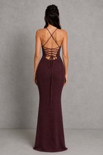 Woman wearing a burgundy evening gown with a lace-up back against a gray background