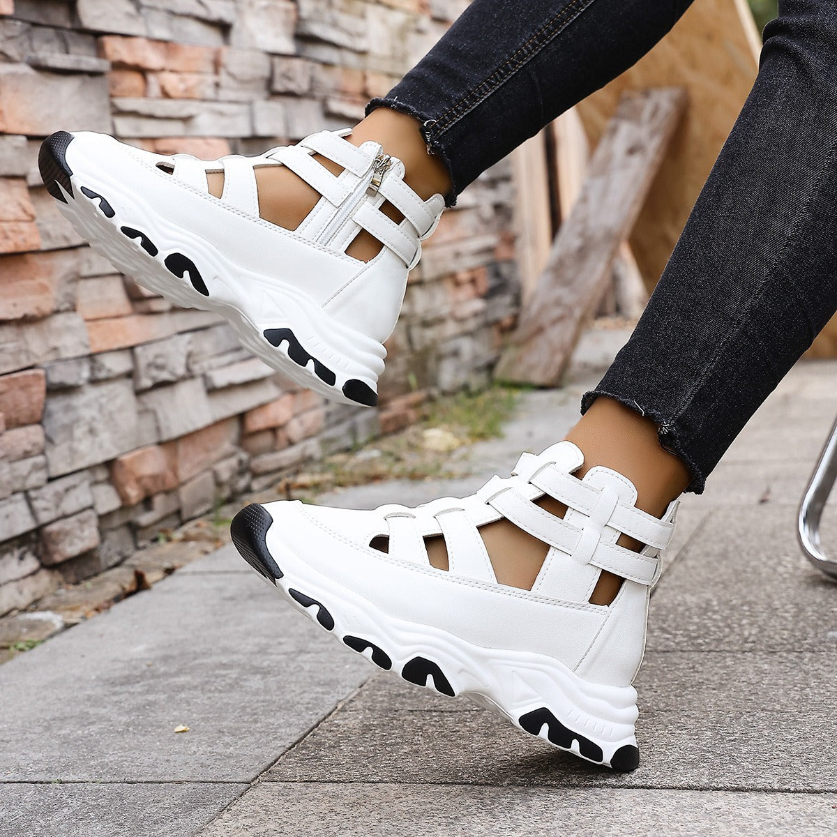 White sandals with black accents worn by a person on a stone pavement.
