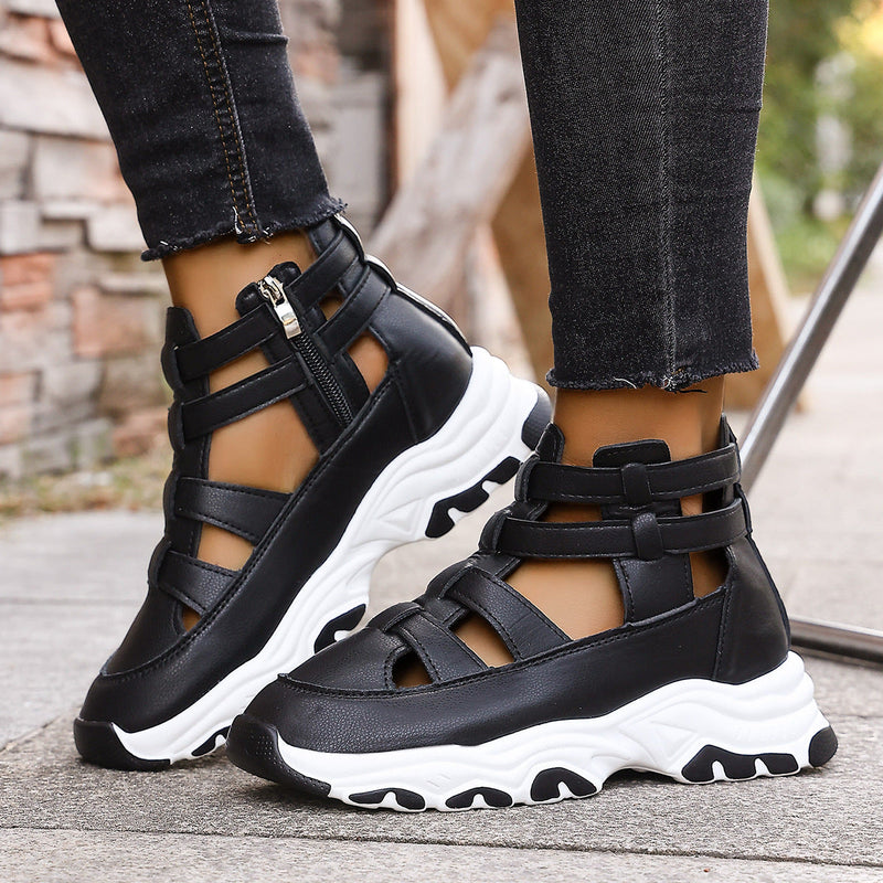 Black strappy sandals with white soles worn by a person on a sidewalk.