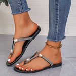 Black sandals with decorative straps worn with blue jeans on a gray floor.