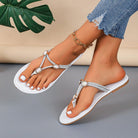 White sandals with embellishments worn by a person on a gray surface with a green leaf in the background