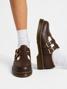Brown shoes with gold buckles worn with white socks on a white background