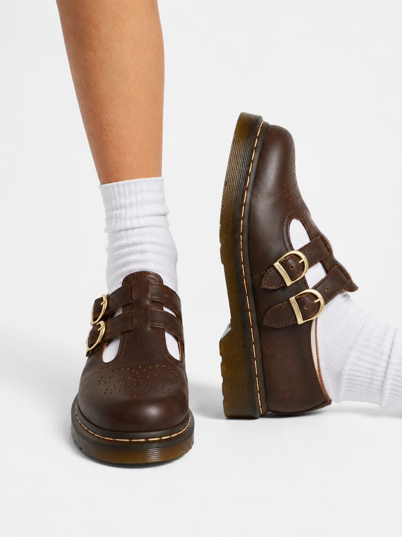 Brown shoes with gold buckles worn with white socks on a white background