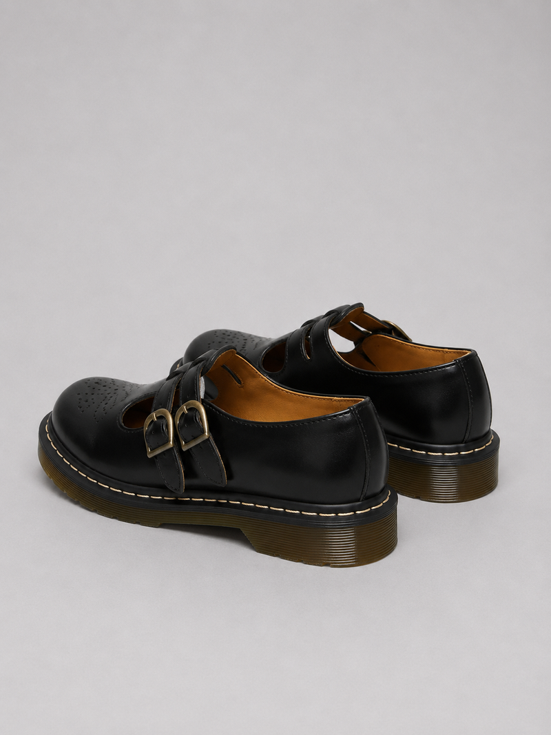 Black leather shoes with buckle details on a light gray background