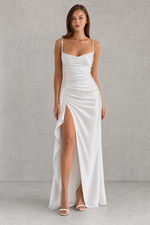 Woman wearing a white evening gown with a high slit on a gray background