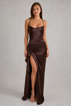 Woman wearing a brown evening gown with a slit on a gray background