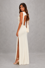 Woman wearing a white evening gown with a high slit on a gray background