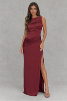 Woman wearing a burgundy evening gown with a slit on a gray background