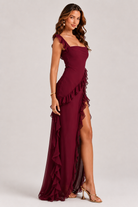 Woman wearing a burgundy evening gown with ruffles on a white background