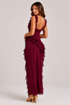 Woman wearing a burgundy evening gown with ruffled details on a white background