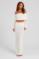 Woman wearing a white off-shoulder top and skirt set against a plain background
