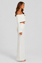 Woman wearing a white off-shoulder top and skirt set against a plain background