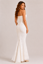 Woman wearing a white strapless gown with a fitted design on a plain background
