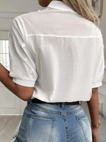Person wearing a white button-up shirt with rolled-up sleeves and blue jeans indoors.