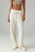 Person wearing white ribbed lounge pants on a wooden floor.