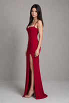 Woman wearing a red evening gown with a high slit on a plain background