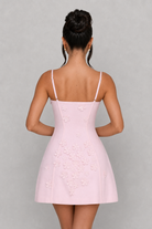 Woman wearing a light pink dress with thin straps on a gray background
