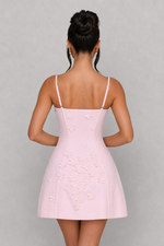 Woman wearing a light pink dress with thin straps on a gray background