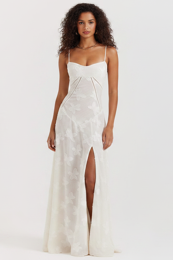 Woman wearing a white slip dress with a high slit on a plain background