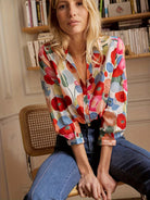 Woman wearing a colorful floral blouse sitting in a chair with bookshelves in the background