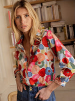 Woman wearing a colorful floral shirt in a room with bookshelves.