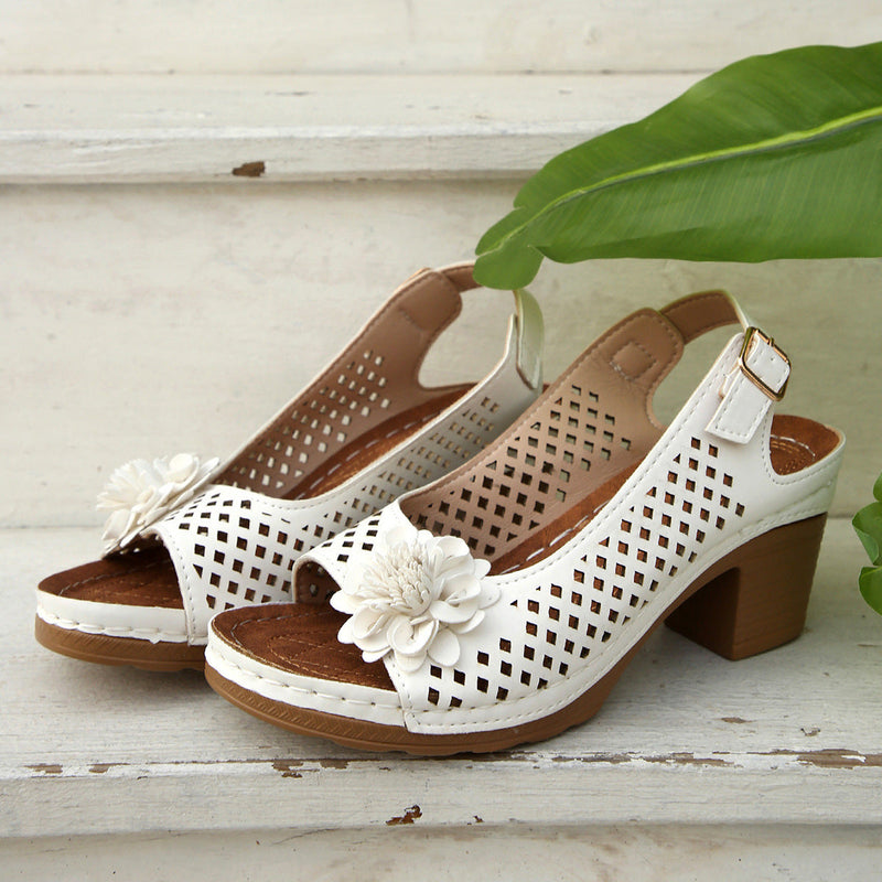 Pair of white and brown open-toe shoes with floral decorations on a wooden surface.