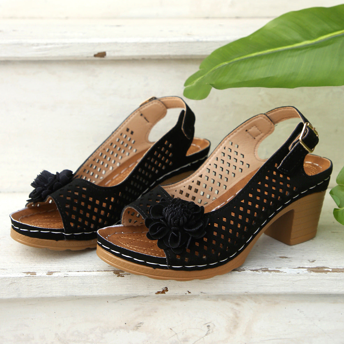Black perforated sandals with floral details on a wooden surface