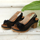 Black perforated sandals with floral details on a wooden surface