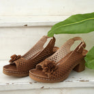 Brown sandals with floral details on a wooden surface with a leaf in the background