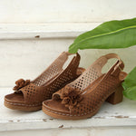 Brown sandals with floral details on a wooden surface with a leaf in the background