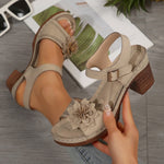 Beige sandals with floral details worn by a person, with a magazine and sunglasses in the background.