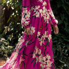 Person wearing a vibrant pink dress with floral and butterfly patterns, standing against a green leafy background.
