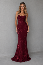 Woman wearing a burgundy lace evening gown against a gray background