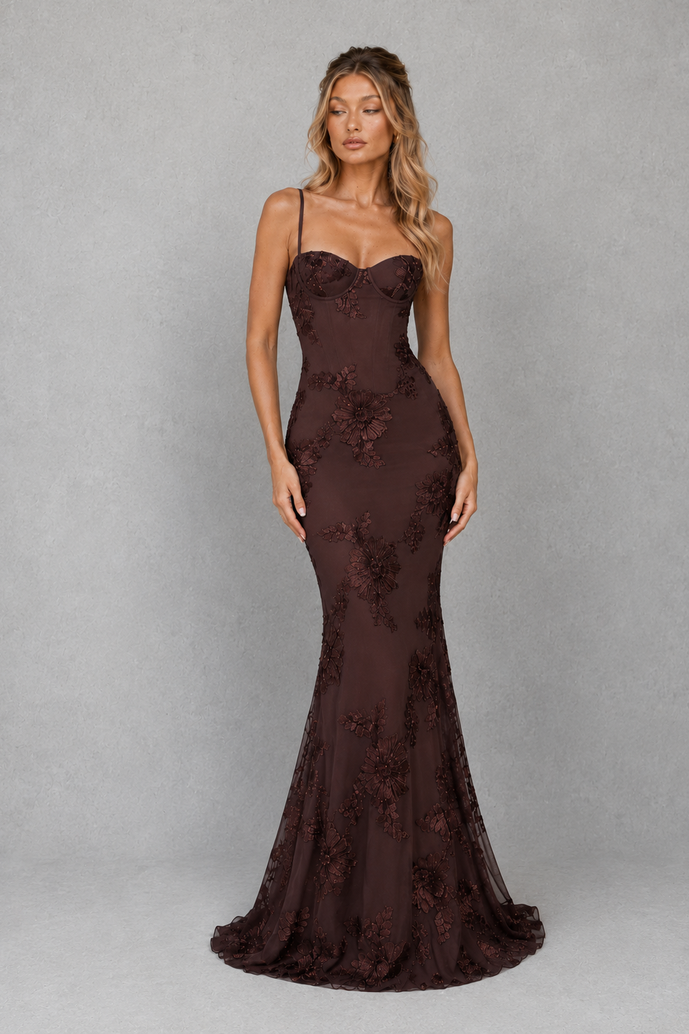 Woman wearing a dark brown evening gown with floral embroidery on a gray background