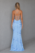 Woman wearing a light blue evening gown with floral patterns against a gray background