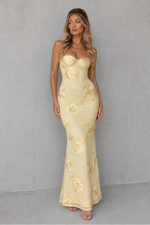 Woman wearing a strapless, light-colored lace dress against a plain background