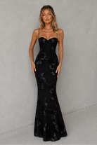 Woman wearing a black floral evening gown against a gray background