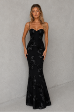 Woman wearing a black floral evening gown against a gray background