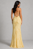 Woman wearing a yellow evening gown with lace-up back against a gray background